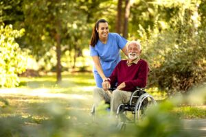 An older adult enjoys a meal in a comfortable assisted living dining room with attentive staff nearby.